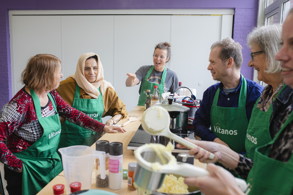 6 mensen zijn aan het koken. Ze praten en lachen.